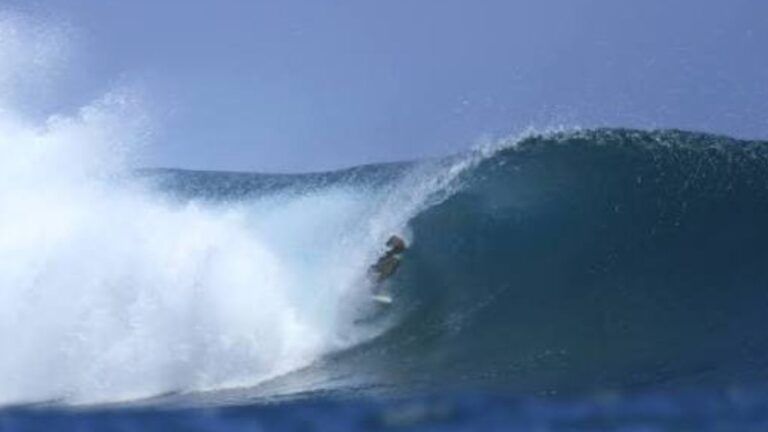 Surfista experimentado surfeando dentro de un tubo azul cristalino con espuma blanca rompiendo a la izquierda.